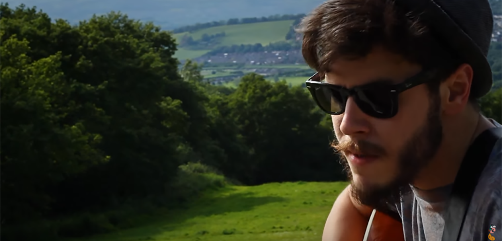 Jon Lilygreen playing his guitar on a hill
