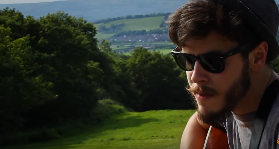 Jon Lilygreen playing his guitar on a hill